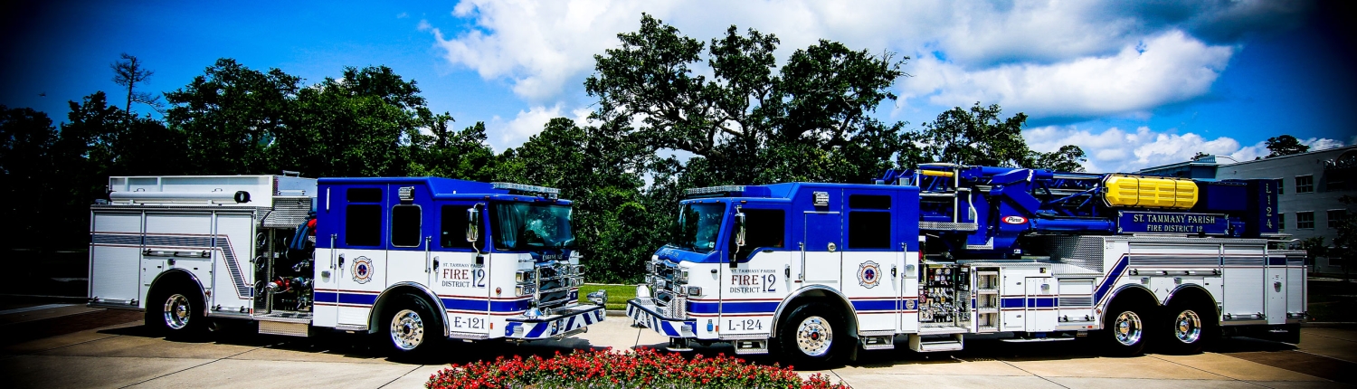two fire engines face to face with sky and clouds and flower garden